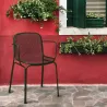 Fauteuil empilable en résille métallique vert foncé devant un mur rouge