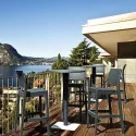 Chaise haute gris foncé aspect tressé autour d'une table mange-debout sur une terrasse extérieure au-dessus d'un lac
